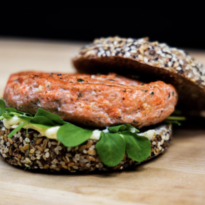 Garlic Salmon Burger with top bun open. Burger contains lettuce on woodtop.