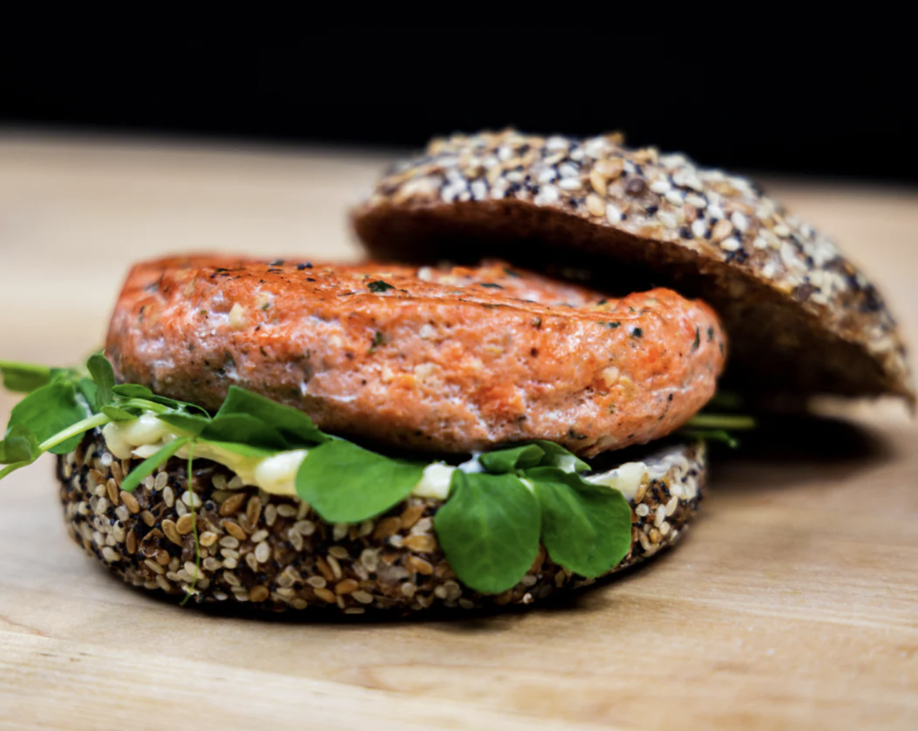 Garlic Salmon Burger with top bun open. Burger contains lettuce on woodtop.
